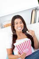 Cheerful asian woman sitting on sofa and eating popcorn