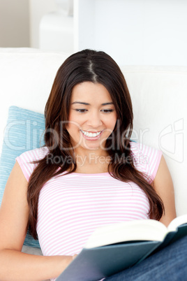 Pretty asian woman sitting on her sofa reading a book