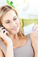 Beautiful young woman holding a card and phoning lying a sofa