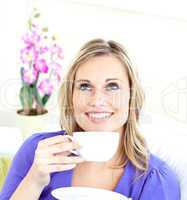 Delighted young woman holding a cup of coffee on a sofa