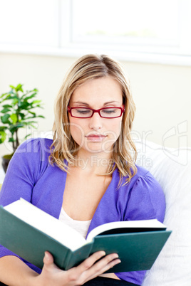 Concentrated young woman wearing red glasses reading a book on a