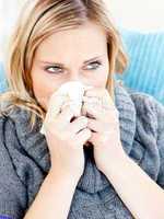 Dejected woman lying on a sofa with tissues and blowing