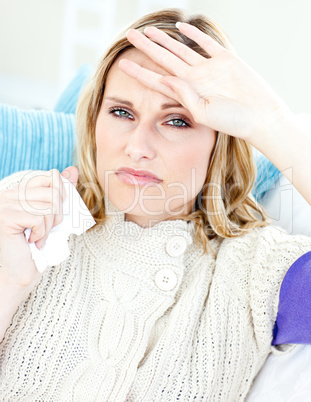 Dejected woman lying on a sofa with tissues and feeling her temp