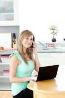Smiling woman on phone using a laptop in the kitchen