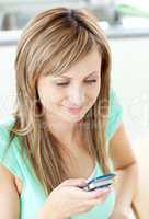 Happy young woman writing a message on her cellphone at home