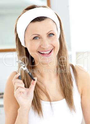 Cheerful woman holding an eyelash curler looking at the camera i
