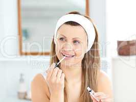 Happy woman applying gloss on her lips in the bathroom