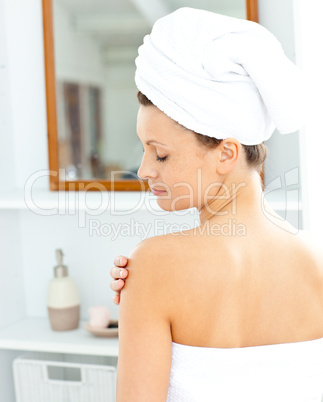 Pleased young woman with a towel putting cream on her face in th
