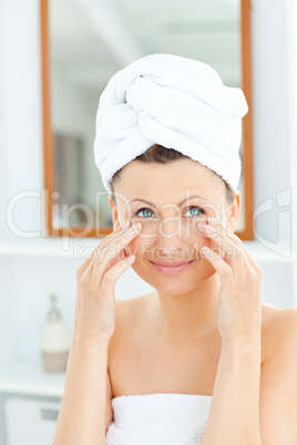 Beautiful young woman with a towel putting cream on her face in