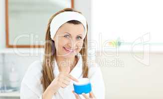 Delighted young woman putting cream on her face in the bathroom