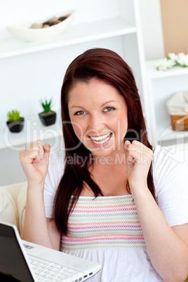 Cheerful young woman using her laptop sitting on a sofa
