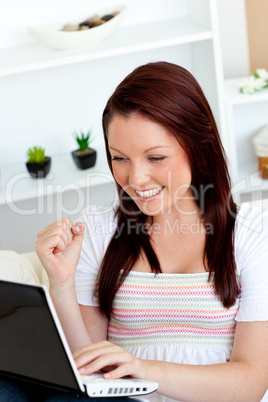 Joyful young woman using her laptop sitting on a sofa