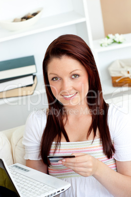 Happy woman with a credit card and a laptop on a sofa
