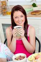 Charming woman eating her breakfast at home holding a cup of cof