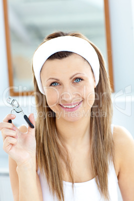 Smiling woman holding an eyelash curler looking at the camera in