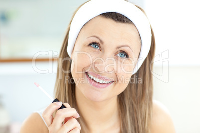 Delighted woman applying gloss on her lips in the bathroom