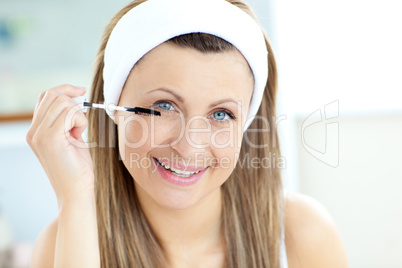 Happy young woman using mascara in the bathroom