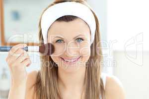 Smiling caucasian woman putting powder on her face smiling at th