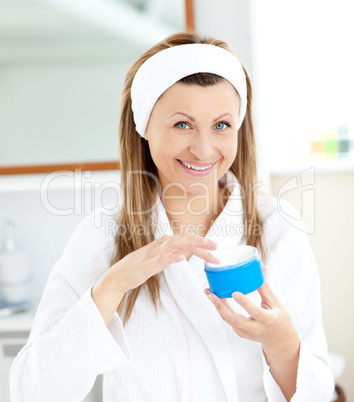 Cute young woman putting cream on her face in the bathroom