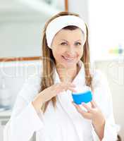 Cute young woman putting cream on her face in the bathroom