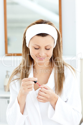 Happy young woman varnishing her fingernails in the bathroom