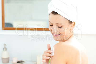 Attractive young woman with a towel putting cream on her face in