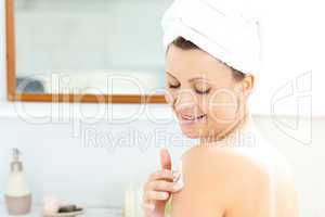 Attractive young woman with a towel putting cream on her face in