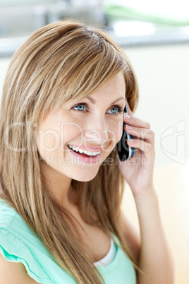 Cheerful woman answering the phone in the kitchen