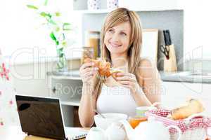 Smiling woman having breakfast in front of the laptop in the kit
