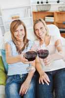 Two bright women holding a wineglass on a sofa