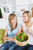 Two female friends eating salad together on a sofa