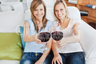 Two cute women holding a wineglass on a sofa