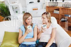 Two cute women drinking coffee together on a sofa