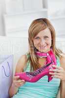 Attractive caucasian woman holding a pink shoe on a sofa