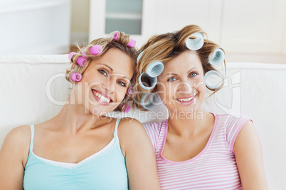 Laughing female friends with hair rollers on a sofa