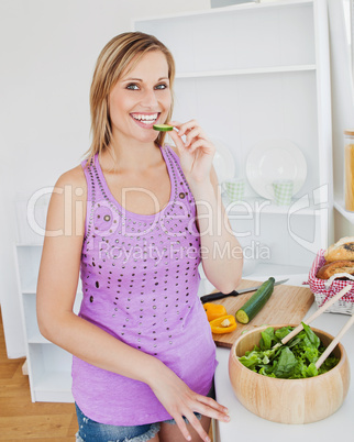 Smiling woman eating cucumber in the kitchen