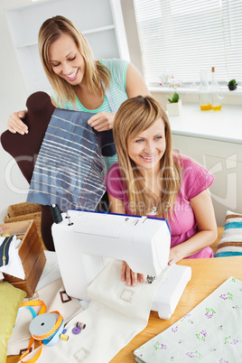 Happy young female friends sewing clothes together at home