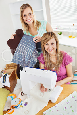 Bright young female friends sewing clothes together at home