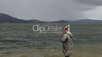 Fisherman with spinning catching fish in mountain lake Dayan Nuur