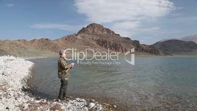 Fisherman with spinning catching fish in mountain lake Tolbo Nuur