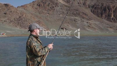 Fisherman with spinning catching fish in mountain lake Tolbo Nuur