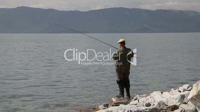Fisherman with spinning catching fish in mountain lake Tolbo Nuur