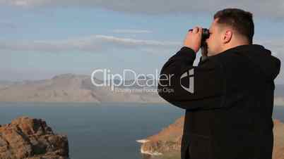 Hiker in mountain look into binoculars