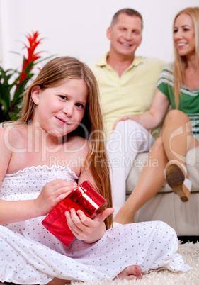 Cute girl opening christmas gift with parents in the background