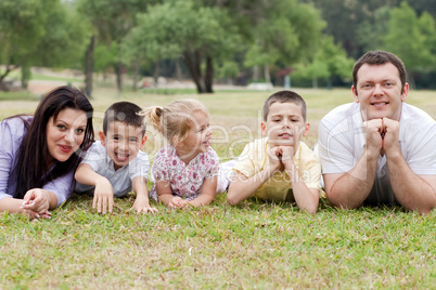 Cheerful family of five lying on lawn in the green park