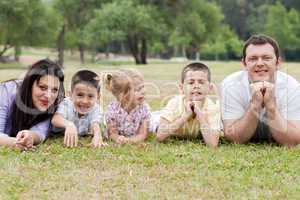 Cheerful family of five lying on lawn in the green park