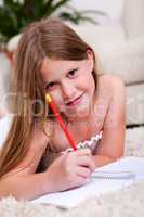 Smiling young girl lying and writing in notebook