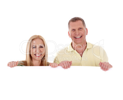 Middle aged couple standing behind a blank white board and smiling