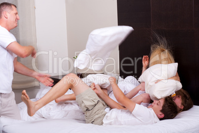 Happy family playing with pillows on the bed