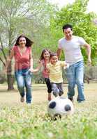 Parents and two young children playing soccer in the green field